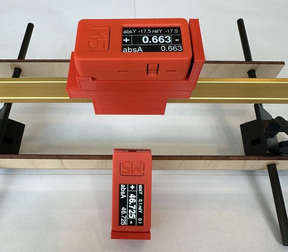 Two 2024-generation gauges in printed red mounts clipped to a rigging jig, each showing absolute and relative angle readings.
