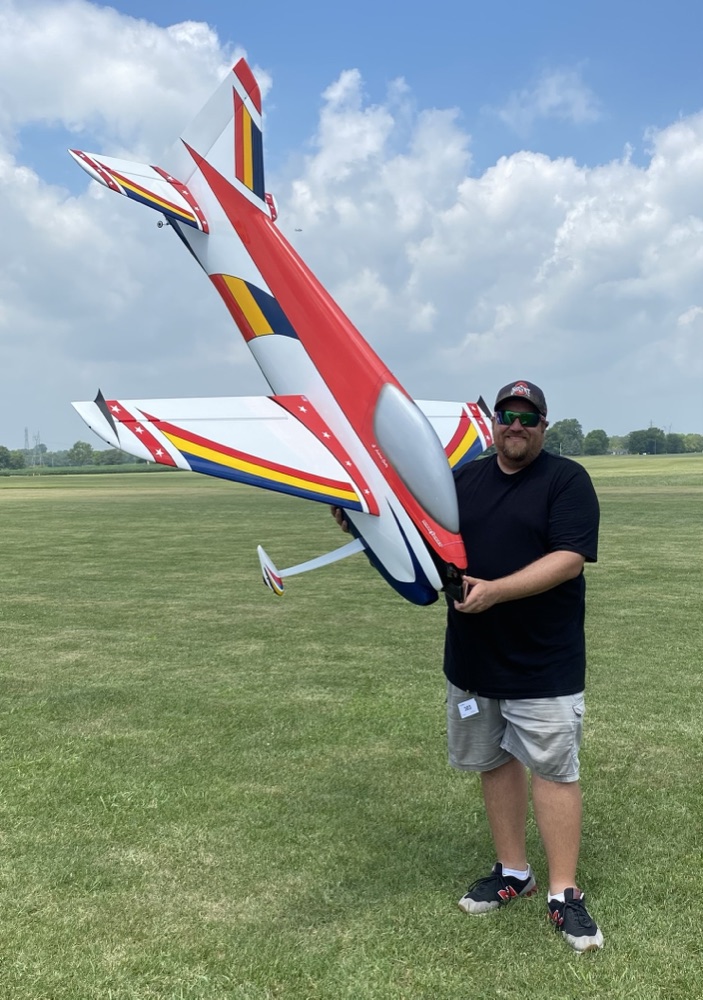 Jon Dieringer at a flying field holding a large red and white F3A aerobatic aircraft.